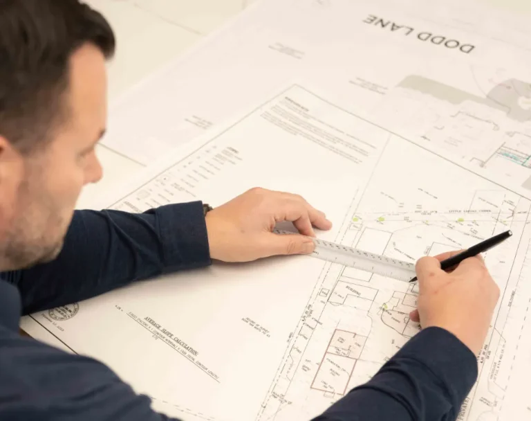 Architectural design professional reviewing residential building plans with a ruler and pen