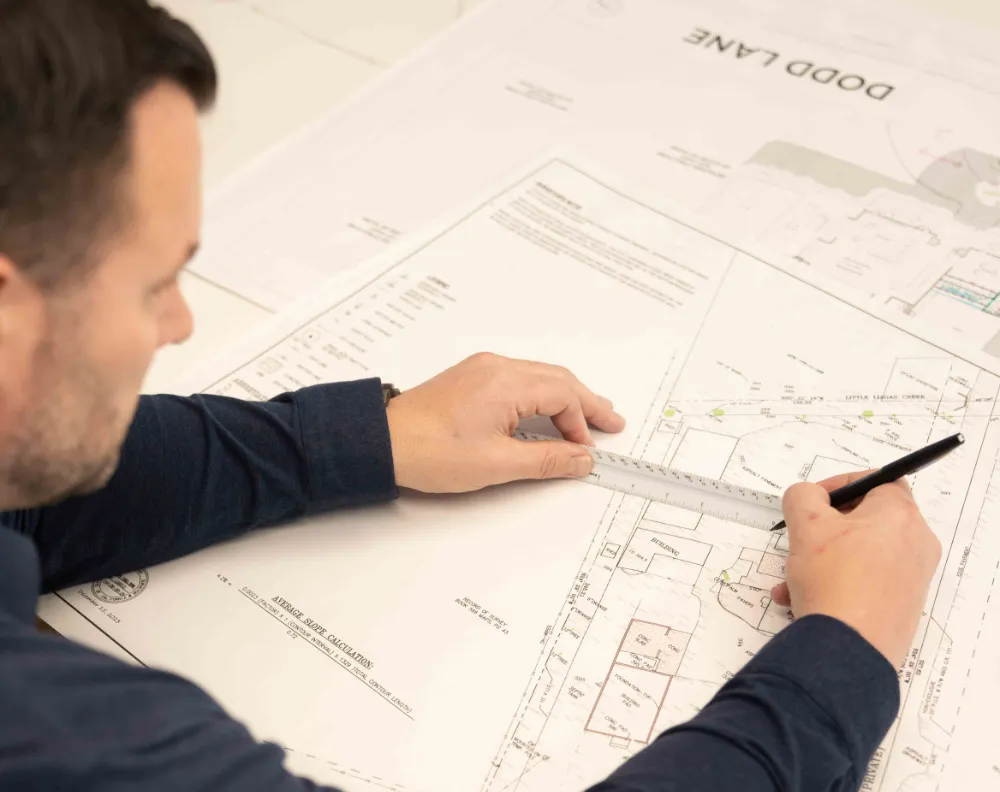 Architectural design professional reviewing residential building plans with a ruler and pen