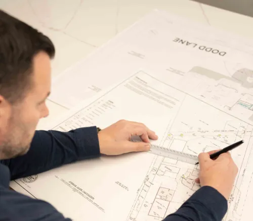 Architectural design professional reviewing residential building plans with a ruler and pen