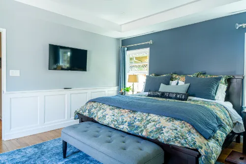 Residential construction project with a finished bedroom, blue accent wall, wood flooring, and custom wall trim